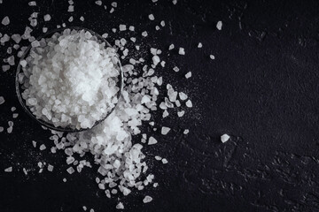 White sea salt in steel bowl on black background. Top view.