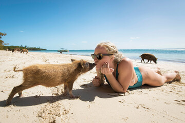 Young woman kissing piglet while lying on sand at beach during summer vacation
