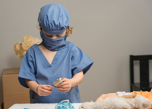 Young Child Wearing Medical PPE Prepares Syringe Before Administering Shot To Toy Patients