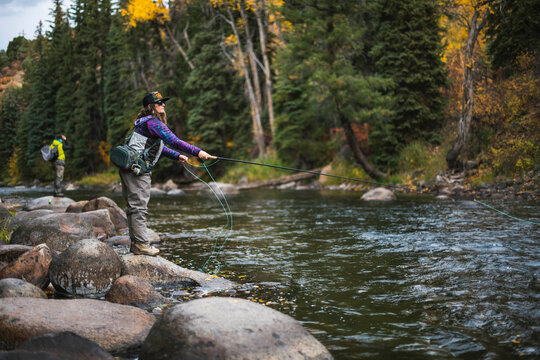 Side view of woman fly fishing while standing on rock at Roaring Fork River - Powered by Adobe