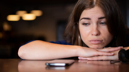 The sad woman has laid her head on the table and is waiting for a phone call