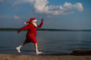 Santa Claus in shorts runs along the beach. Concept of celebrating christmas at sea
