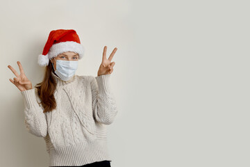 Young beautiful woman wearing red santa hat and protection mask over isolated beige background doing victory sign. Number two