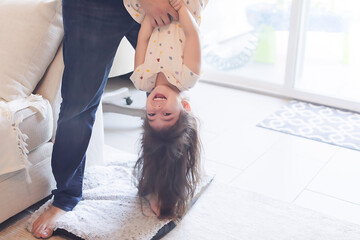 Dad holding daughter upside down in the living room.