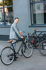 Fototapeta premium Cheerful businessman with takeaway coffee standing near bicycle parking outdoors