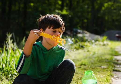 Young boy blowing soap bubbles with a large wand outdoors.
