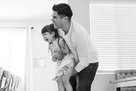 Black and white photo of dad holding daughter, both laughing.