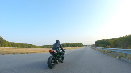 Obraz premium Follow to motorcyclist in helmet riding on sport motorbike at highway. Man racing his motorcycle on autumnal country road. Guy driving bike during trip. Concept of freedom and adventure. Aerial shot
