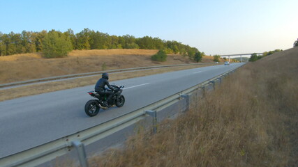 Aerial shot of man riding on modern sport motorbike at autumn highway. Motorcyclist racing his motorcycle on country road. Guy driving bike during trip. Concept of freedom and adventure. Above view