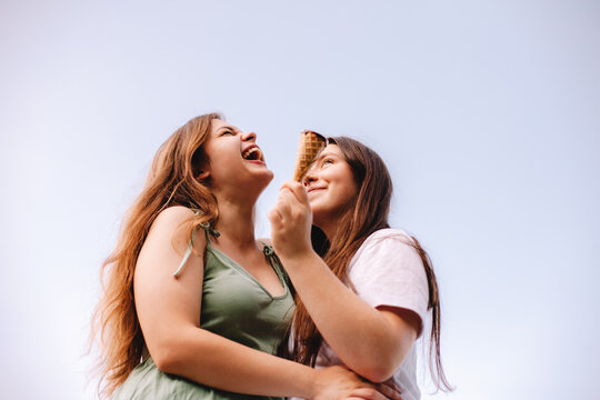 Young woman laughing while embracing her girlfriend against sky