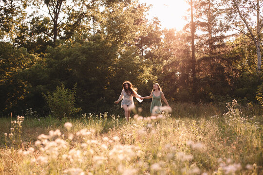 Happy lesbian couple holding hands while running in forest in summer