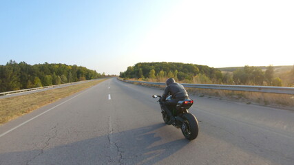 Biker riding on modern sport motorbike at highway during sunny autumn day. Motorcyclist racing his motorcycle on country road. Guy drive bike during trip. Concept of freedom and adventure. Aerial shot