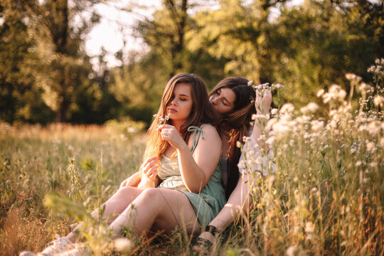 Lesbian couple sitting in field of flowers in forest during summer