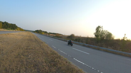 Man riding on modern sport motorbike on country road at sunny day. Motorcyclist racing his motorcycle at highway. Guy drive bike during trip. Concept of freedom and adventure at travel. Aerial shot