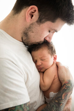 Close Up Side View Of Tattooed Millennial Dad Kissing Newborn Son