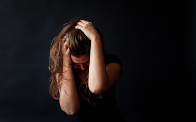 Distressed woman with long brown hair holding her head in her hands.