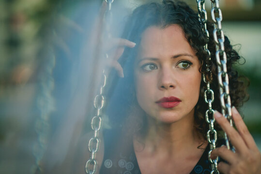 Portrait of a young woman looking at camera. She is sitting on a swing