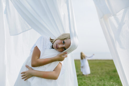 Country children play with washed sheets in summer