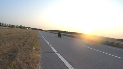 Follow to biker riding on modern sport motorbike on country road at sunset. Motorcyclist racing his motorcycle at highway. Guy driving bike during trip. Concept of journey and freedom. Aerial shot