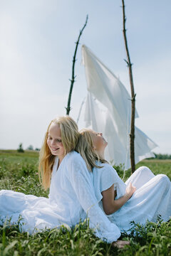 two fair-haired girls in the summer sit on the grass and laugh