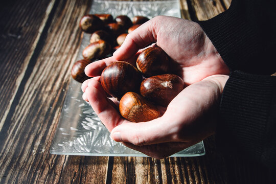 Hands of a woman holding various chestnuts. In the background a plate