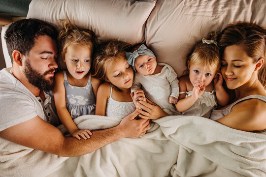 Large family laying in bed with many children and holding hands