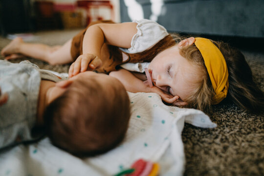 Preschool girl sleeping on floor with baby and sucking on a pacifier