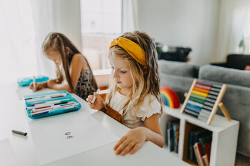 Two girls drawing with colorful markers and paper and smiling at work