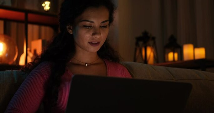 Woman using laptop sitting on sofa late night at home