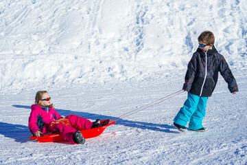 Brother pulling his sister kids toboggan sled snow. Little girl and boy enjoying sleigh ride. Child sledding. Children play outdoors in snow.