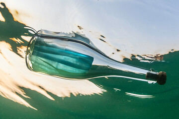 Covid-19 face mask inside a glass bottle floating in the ocean
