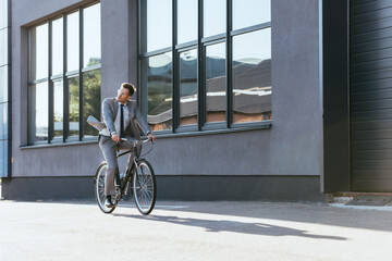 Young businessman riding bicycle near building outdoors