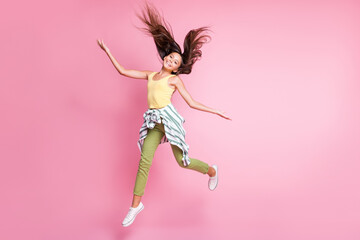 Fototapeta na wymiar Full length photo of positive cheerful child girl dressed casual outfit jumping hands arms sides isolated pastel pink color background