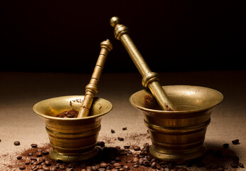 
bronze mortar and pestle, with natural coffee beans and ground powder, on raffia cloth and black...