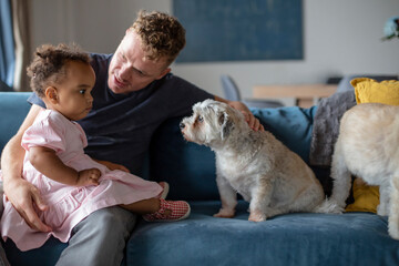 A caucasian father sits with his biracial daughter and puppy