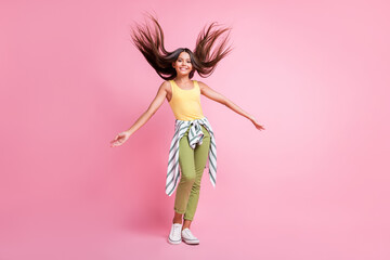 Obraz na płótnie Canvas Full length photo of happy little girl spring wind blow hair wear green pants isolated on pastel pink color background