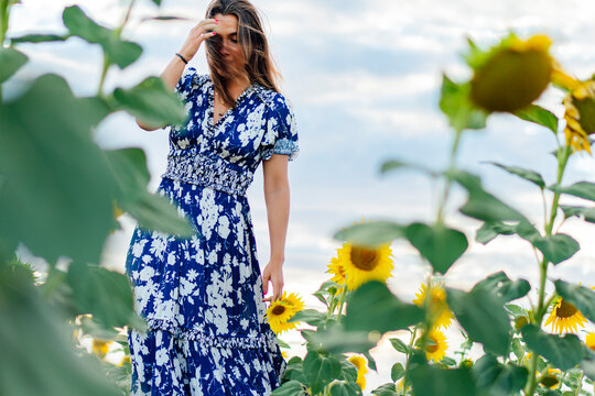 Young attractive brunette woman posing in her designer dress in a field of sunflowers