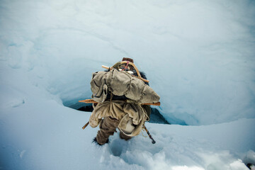 Mountaineer approaches a steep hole, access to ice cave.