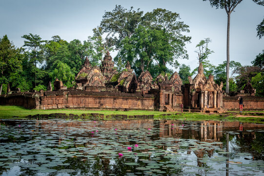 Angkor archaeological Park, Siem Reap, Cambodia. Tourist takes photograph of east entrance yo Banteay Srey temple with lous flowers in moat as foreground.