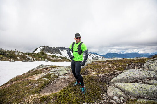 Portrait of trail runner, happily running in the alpine on cloudy day.
