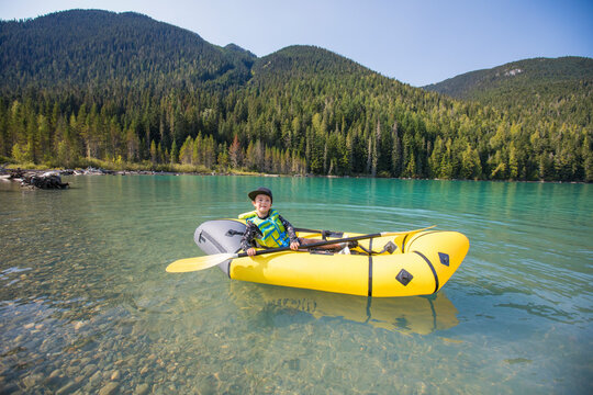 young boy paddling yellow packraft boat on scenic lake near Whistler.