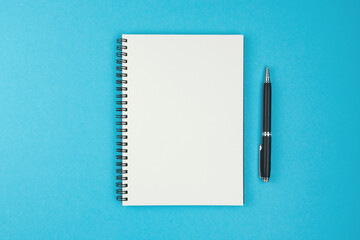 directly above view of blank spiral bound notebook and ballpoint pen on blue background