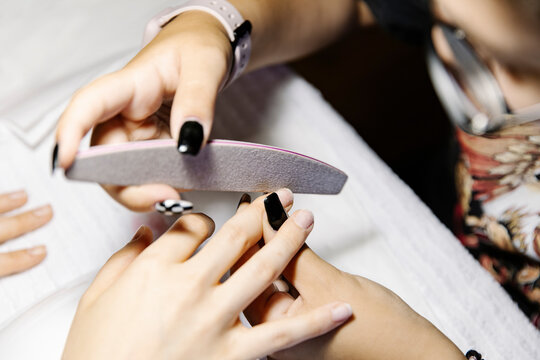 Anonymous woman stylist using file to shape nails of female customer