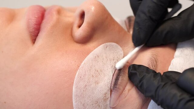Closeup view 4k video of female face of young girl and professional cosmetologist doing modern spa cosmetic procedures of lashes lamination and tinting.