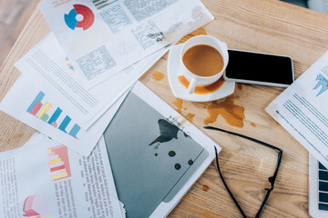 Top view of pouring out coffee near messy papers, eyeglasses and smartphone on table