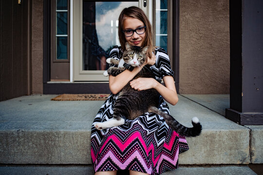 a pre teen girl holding her gray cat on the front porch