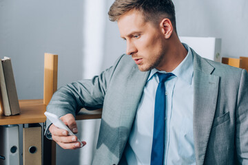 Businessman using smartphone near cupboard with paper folders