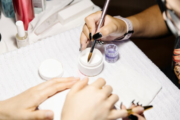 Crop nail artist taking acrylic product from jar while making manicure