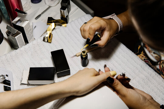Anonymous stylist applying nail polish while making manicure to client