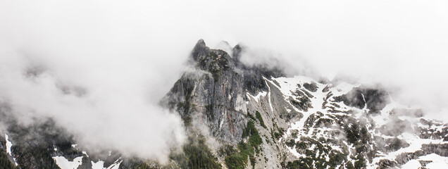 Dramatic mountain peak surrounded by clouds on wet day
